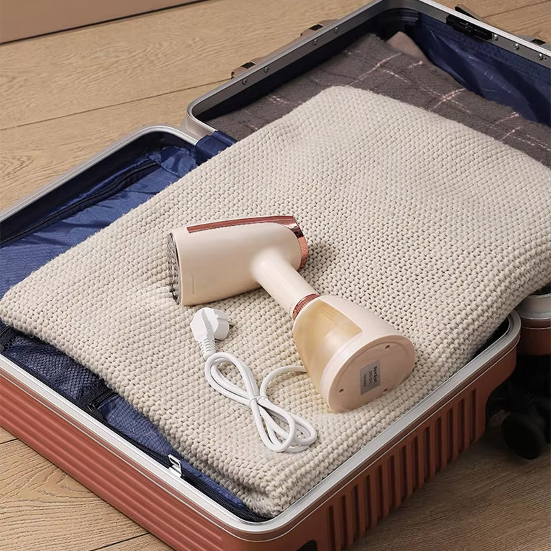 CriisMist Handheld Steamer and its cord on a folded blanket inside an open suitcase.