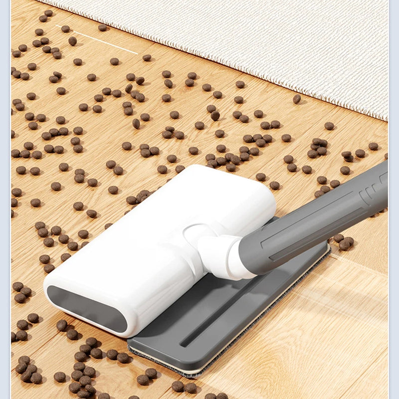 A DustiTrix Cordless Vacuum Cleaner attachment with a white body and gray handle, shown sucking up brown dog kibble from a light wood floor next to a white rug.
