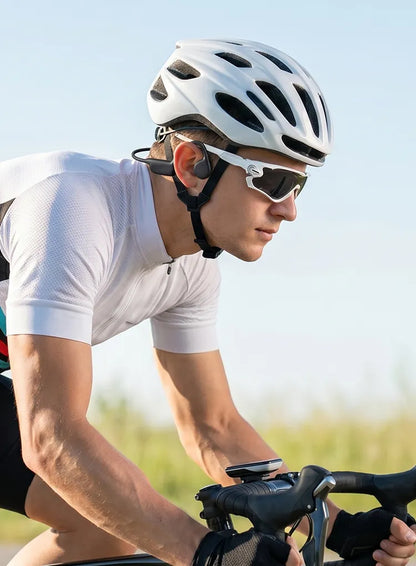 A close-up lifestyle shot of a cyclist wearing a white cycling jersey, a white helmet, and white sunglasses while riding a road bike outdoors.