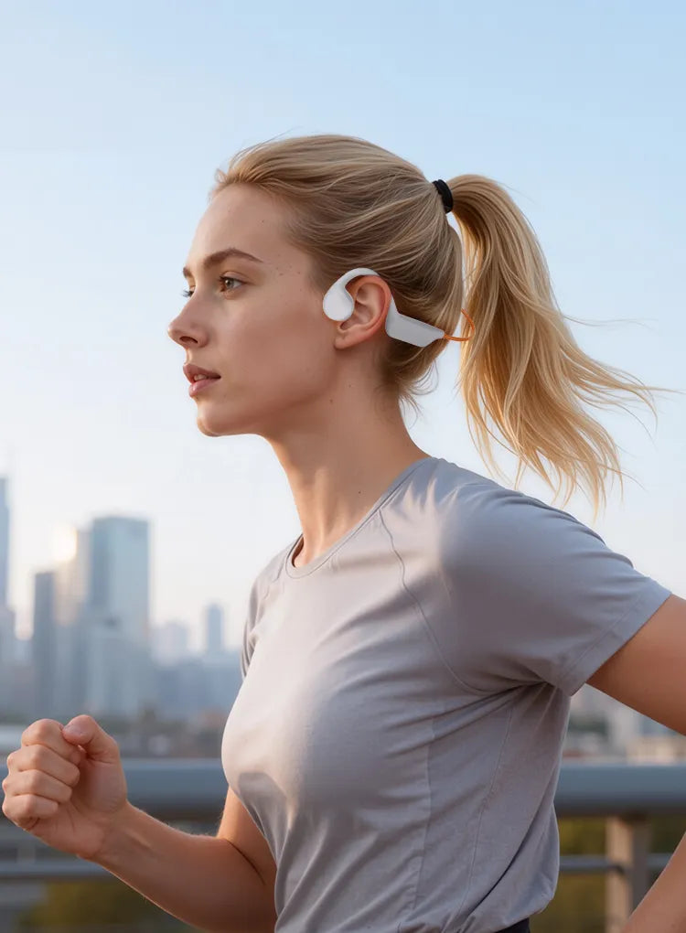 A woman jogging outdoors wearing a white over-ear wireless earbud behind her ear, with a blurred city skyline in the background.