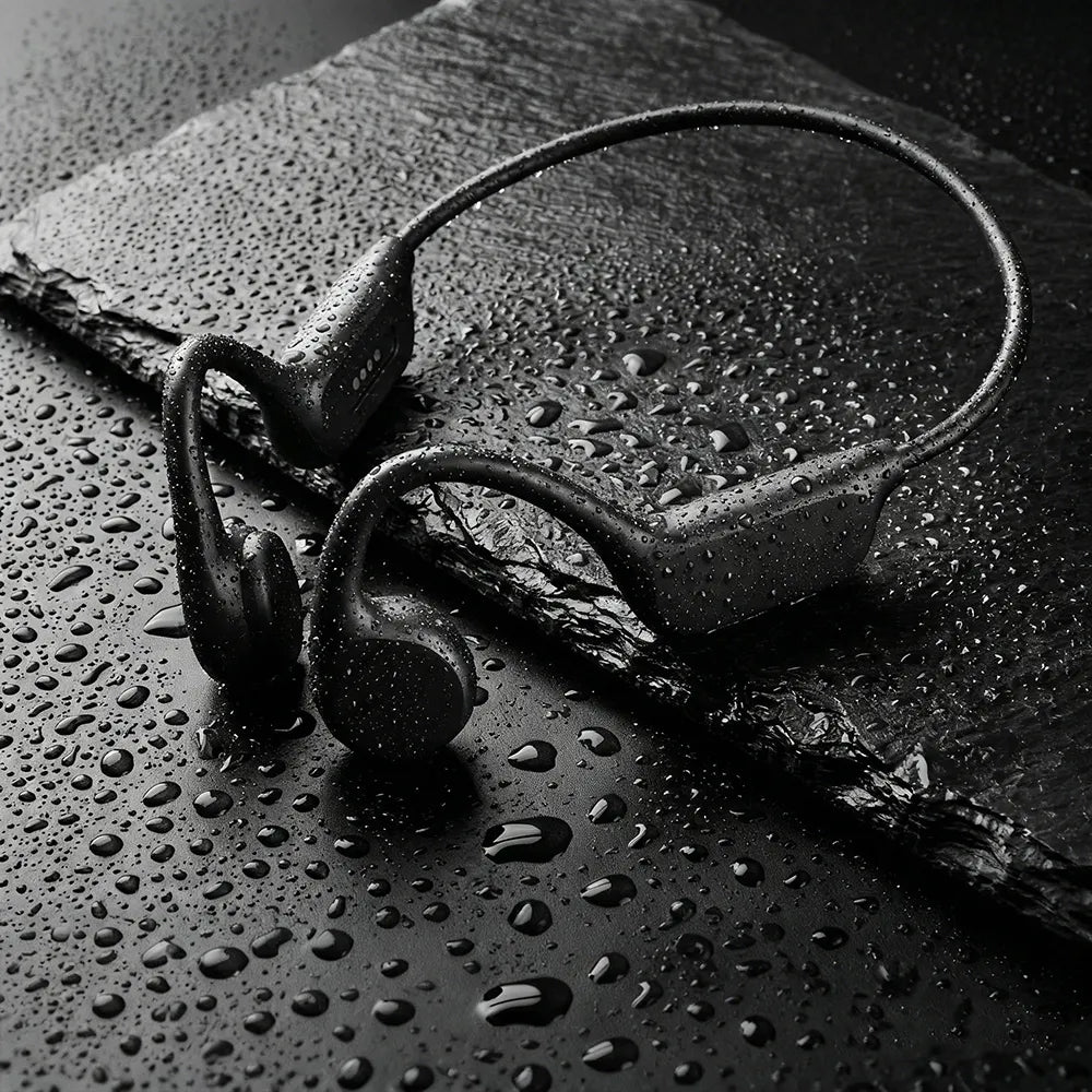 Black sport Audionex Bone Conduction Headphones with a continuous headband, shown with water droplets on a dark slate surface.
