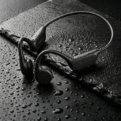 Black sport Audionex Bone Conduction Headphones with a continuous headband, shown with water droplets on a dark slate surface.