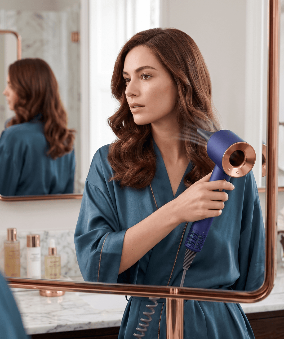 Woman using a Aurevia Smart Ionic Hairdryer in front of a mirror in a bathroom setting