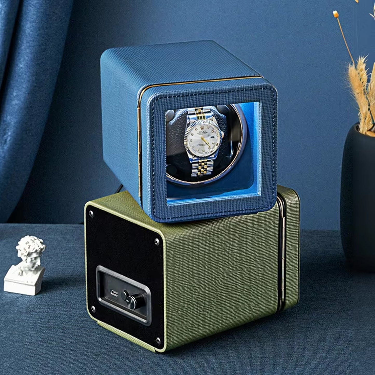 Blue ChroniNova Watch Winder with a watch inside, placed on a dark surface with a blue background.