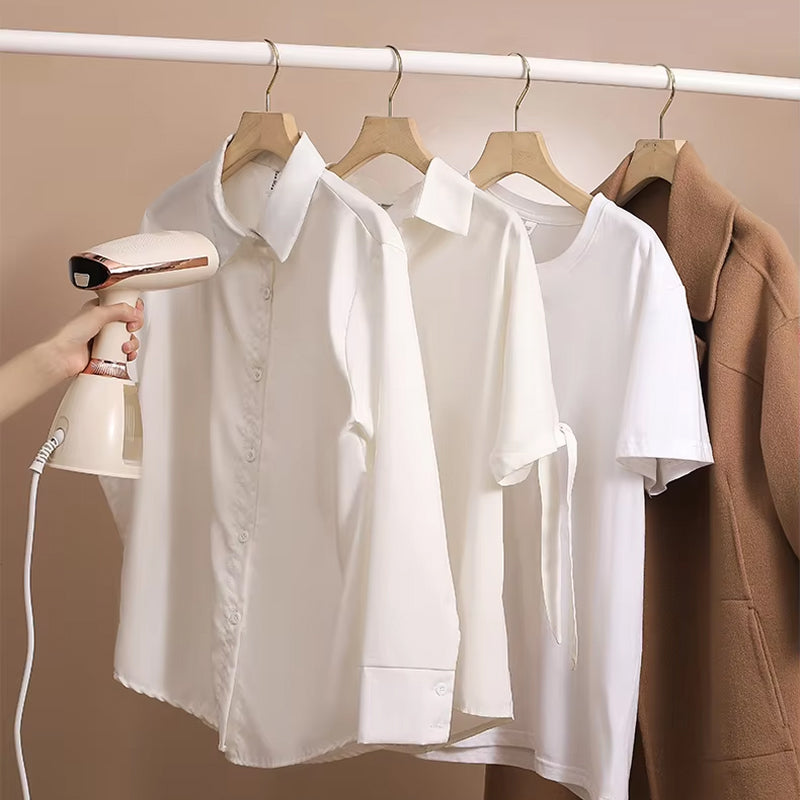White shirts on hangers with a hand holding a CriisMist Handheld Steamer against a beige background