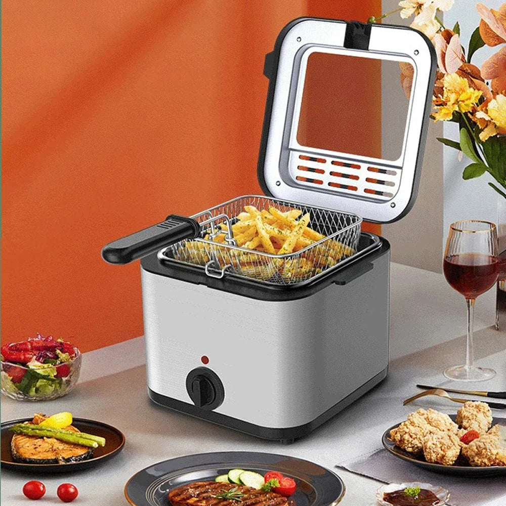 A countertop deep CryspiPro Fryer with a silver and black body, shown with a basket of golden french fries inside. The fryer is placed on a table with plated food, a glass of red wine, and flowers against an orange wall background.