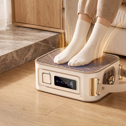 A person wearing cream ribbed socks stands barefoot on the top of a compact Elarvo Shoe & Boot Dryer warmer placed on a wood floor in a living room setting. The warmer is cream-colored with gold-tone accents, a front digital display, and a side handle.