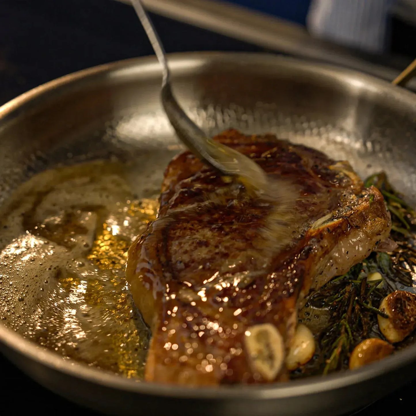 Searing steak in a Ironis Titanium Hammered Pan with herbs and garlic, close-up shot.