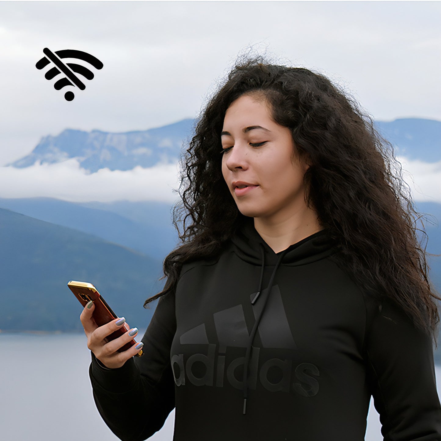Woman in black Adidas hoodie using a phone with mountains in the background
