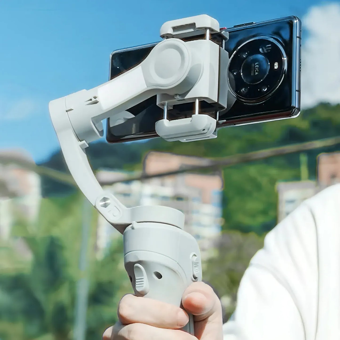 Hand holding a smartphone Optego Gimbal with a clear sky and blurred background