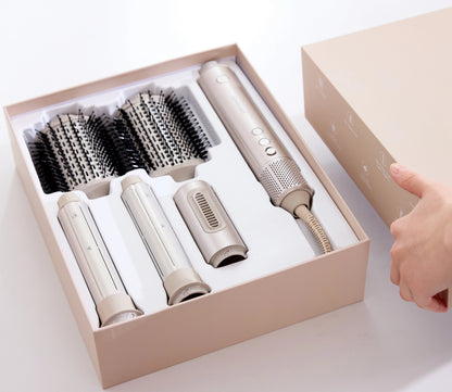 A SaharaCurl RQ30 Automatic 5-in-1 Hot Air Styler in a beige presentation box, including a handheld styler, three brush attachment heads, and two round brush rollers. A hand is visible holding the lid of the box next to it on a clean white background.