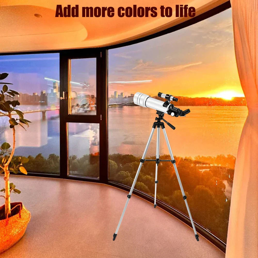 StaryNoxi Telescope on a tripod in a room with a large window view of a sunset.