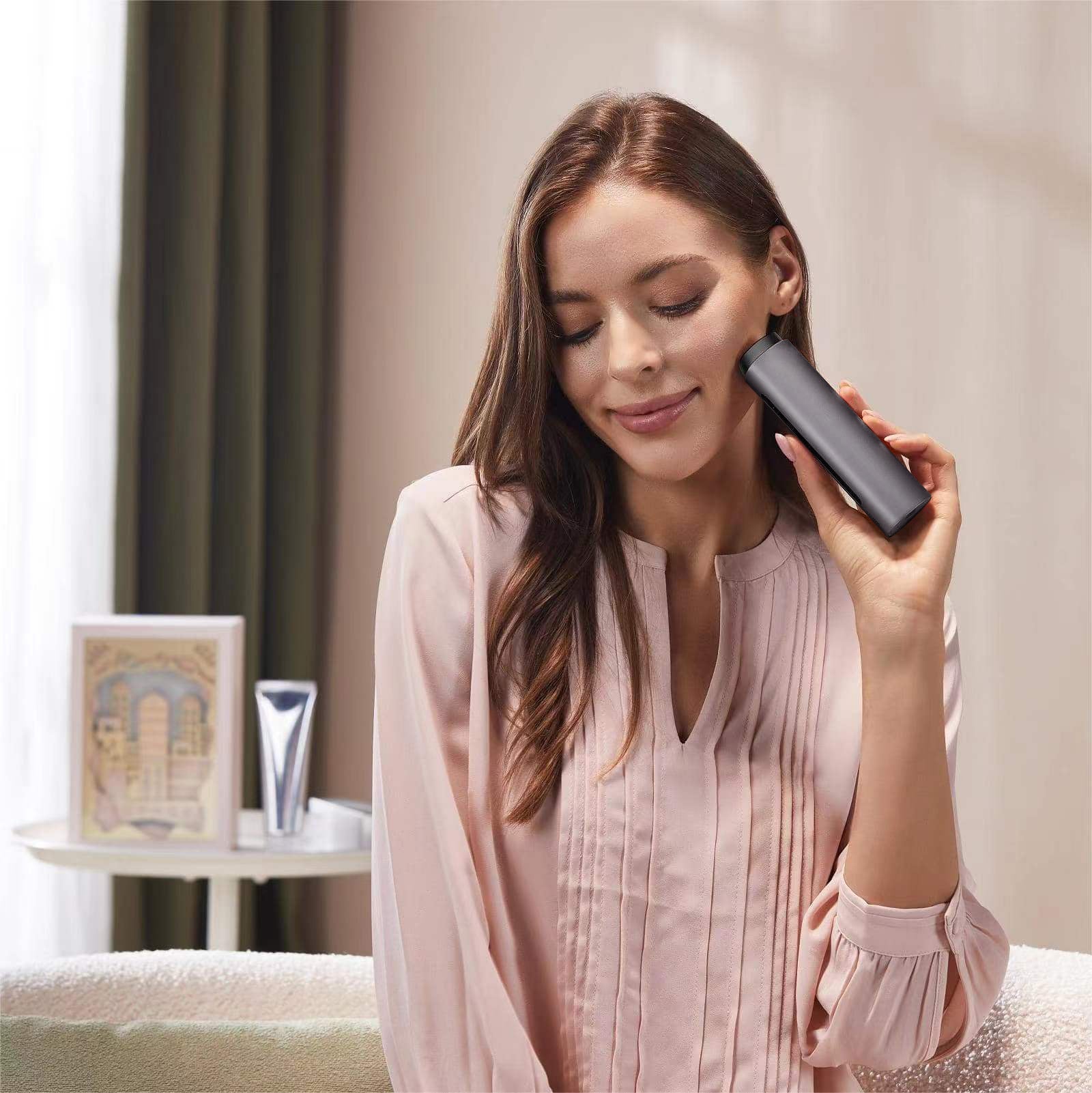 Woman holding a black Vellera S1 Pro Facial Skin Tightening Device in a room with a blurred background