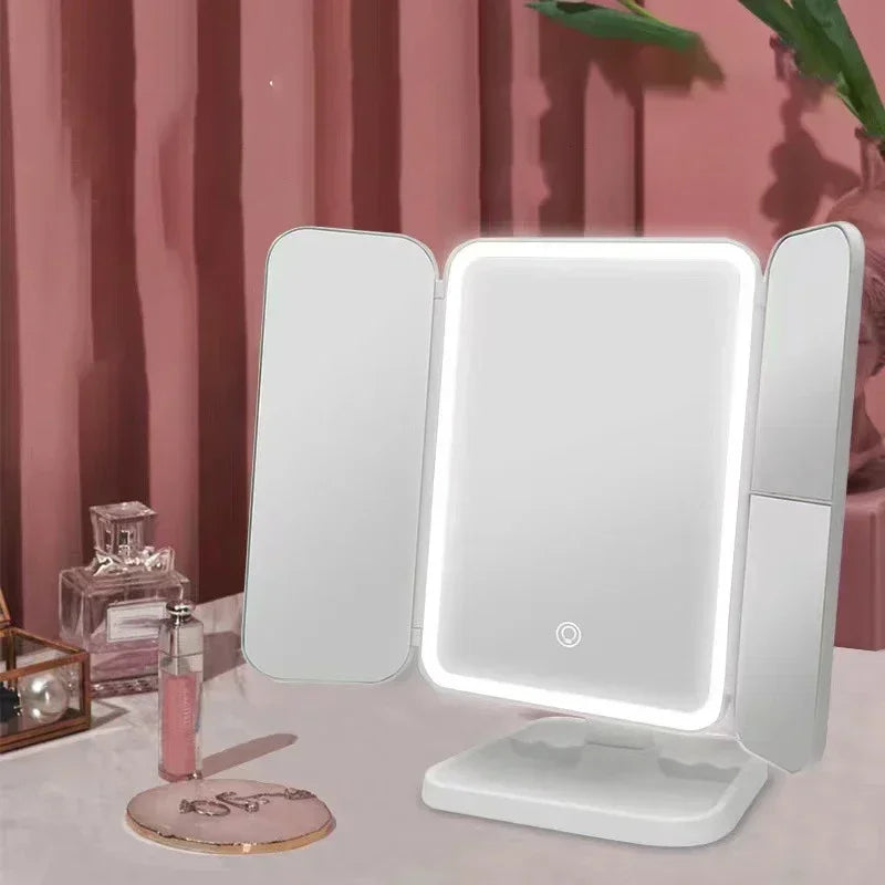 Tri-fold VeloGleam Lighted Makeup Mirror with LED lights on a pink surface with decorative items.