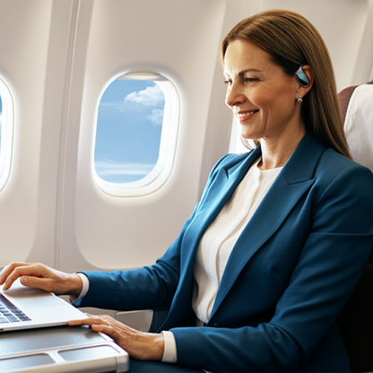 Woman in a blue blazer using a laptop on an airplane with a window view.
